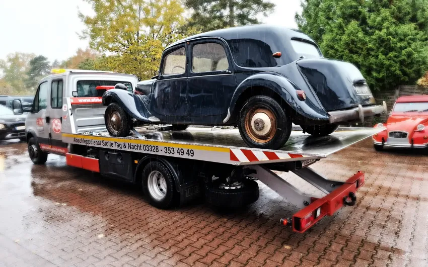 Abschlepp Waagen auf einem Parkplatz mit einem Oldtimer auf der Ladefläche, an einem regnerischen Tag.